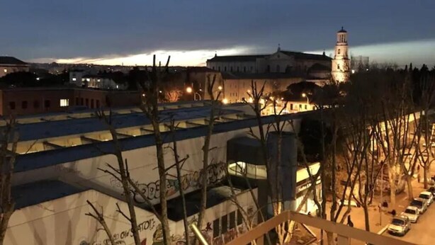 Un edificio con una torre, un estacionamiento y vistas a un atardecer.