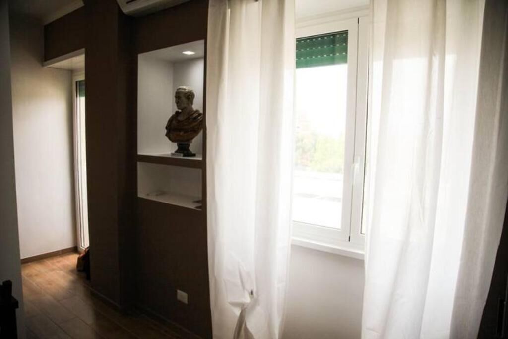 A hallway with a window, a bust sculpture on a shelf, and a door at the end.