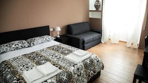 Habitación de hotel con cama, sofá, mesita de noche y espejo.