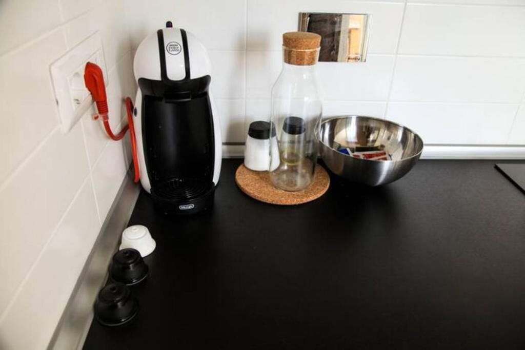 A kitchen with a coffee maker, salt and pepper shakers, a glass bottle, and a metal bowl on a black countertop.