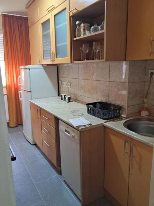 A compact kitchen with wooden cabinets, a white refrigerator, a sink, and a countertop with a dish rack.