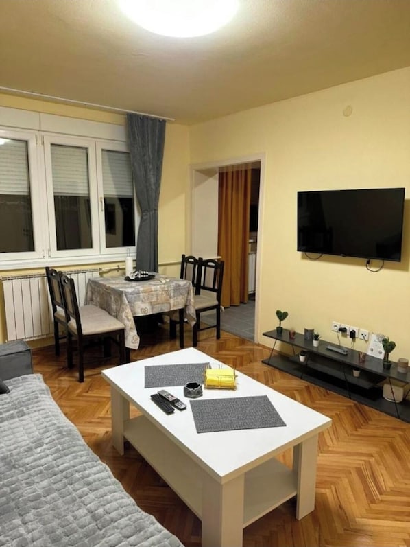 A living room with a dining table, chairs, a flat-screen TV, a coffee table, and a sofa.
