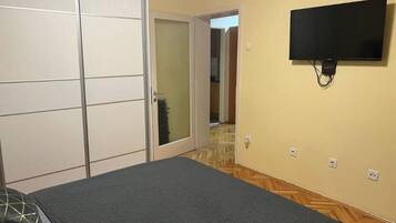 Quarto com cama, TV fixada na parede, guarda-roupa com porta de correr e chão de madeira.
