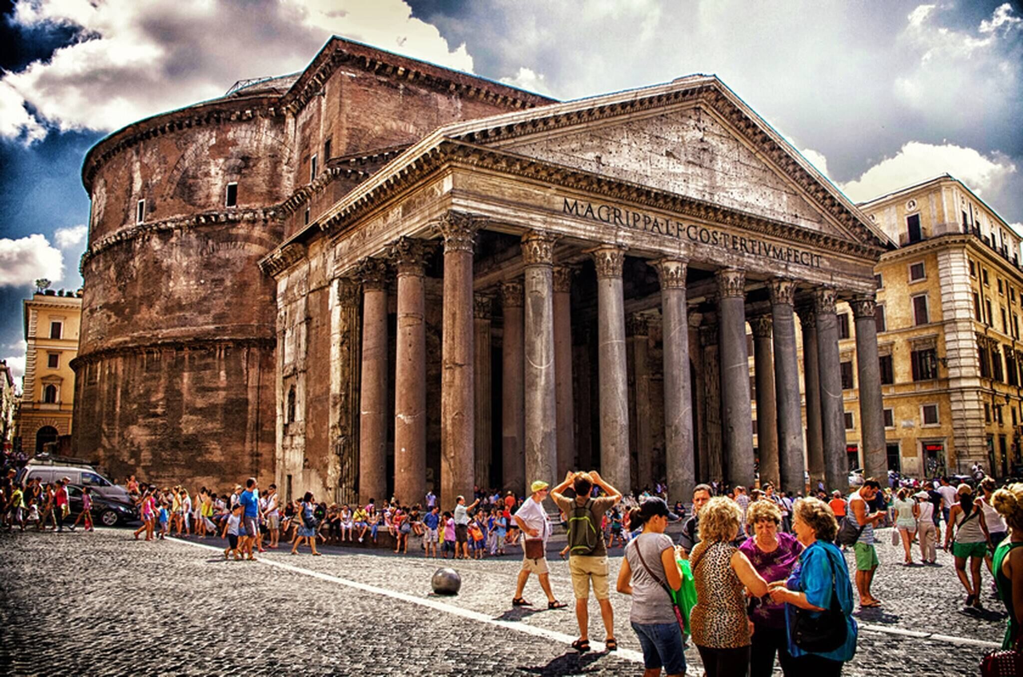 Un bâtiment historique à l’architecture classique, avec des colonnes et un fronton, entouré de touristes.