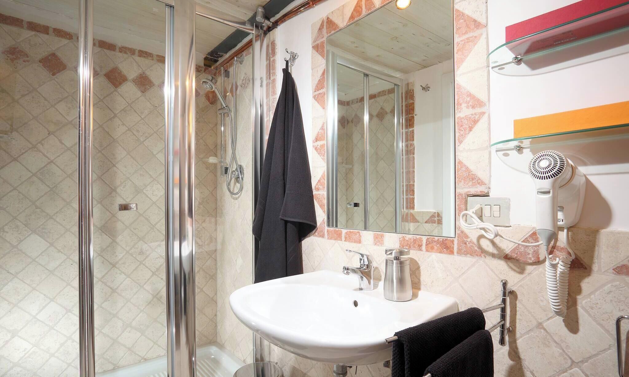 Een badkamer met een douchecabine van glas, een witte wastafel, een spiegel en een haardroger aan de muur.