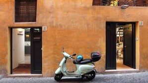 A light green scooter parked on a cobblestone street, with a building featuring two doors and a window with a metal grid. - Manray Charming and Modern Ground Floor Loft (Rome)