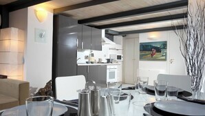 A modern dining area with a table set for two, a kitchen in the background, and a painting on the wall. - Manray Charming and Modern Ground Floor Loft (Rome)