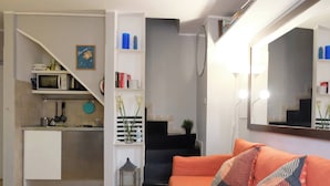 A compact living space with a kitchenette, a sofa with patterned cushions, a staircase, and a mirror. - Mir Small Loft on Giulia Street (Rome)