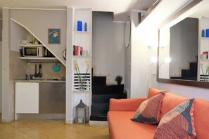 Ein kompakter Wohnraum mit Küchenzeile, einer Couch mit gemusterten Kissen, einer Treppe und einem Spiegel.