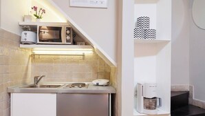 A compact kitchen with a built-in microwave, toaster, and coffee maker, a sink, and a small shelf with decorative items. - Mir Small Loft on Giulia Street (Rome)