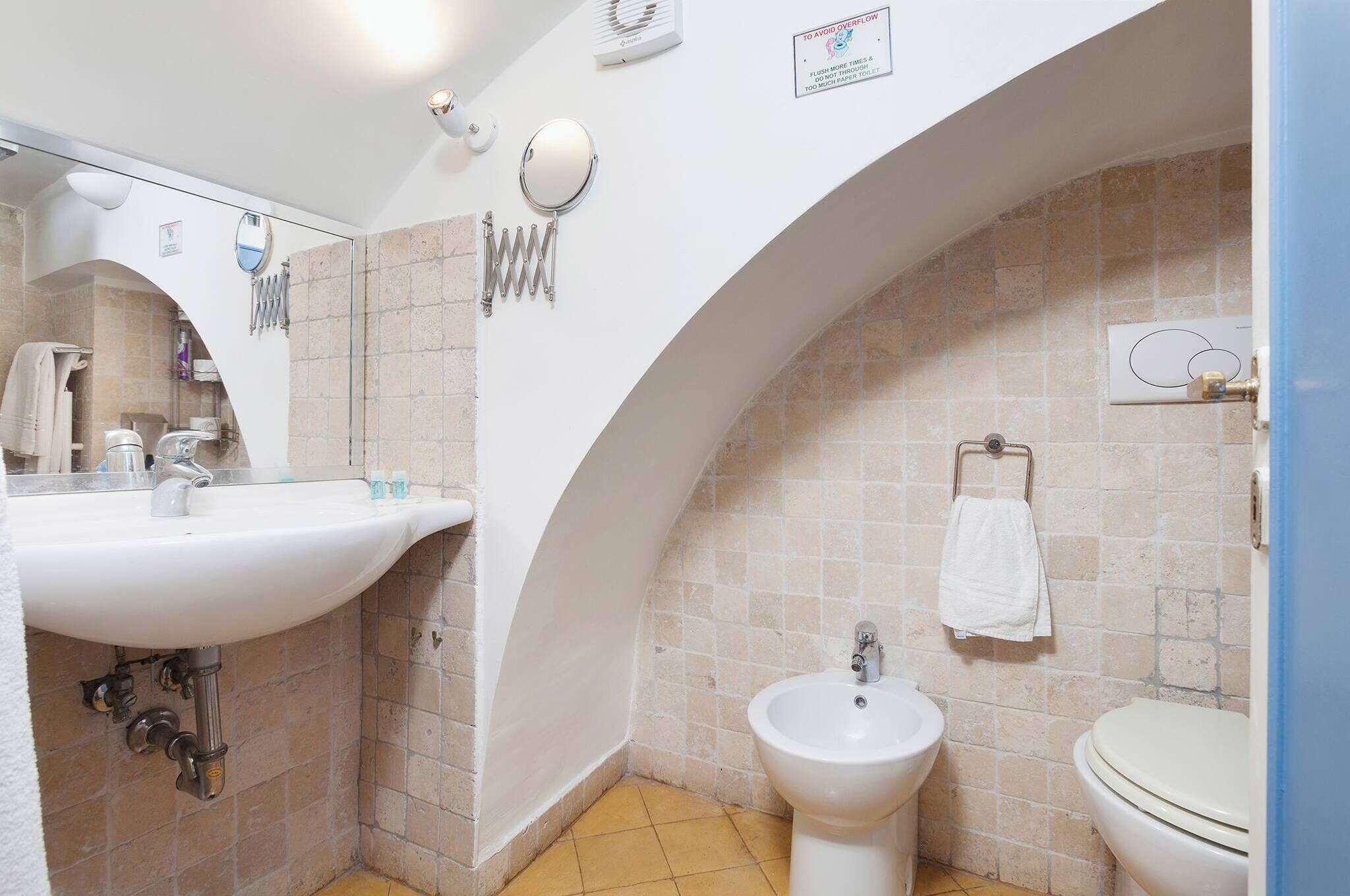 A bathroom with a white sink, bidet, and toilet, tiled walls, and a towel rack.