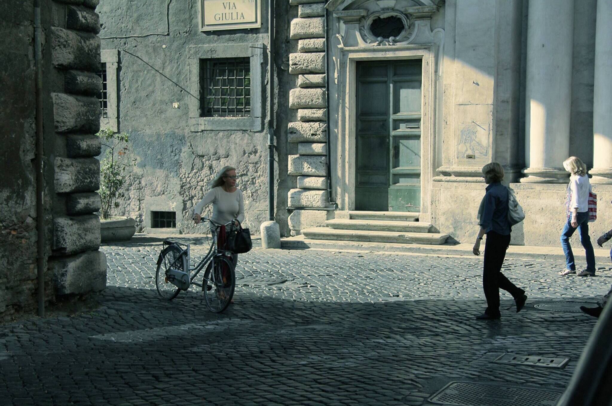 A cobblestone street with a historic building, a bicycle, and pedestrians.