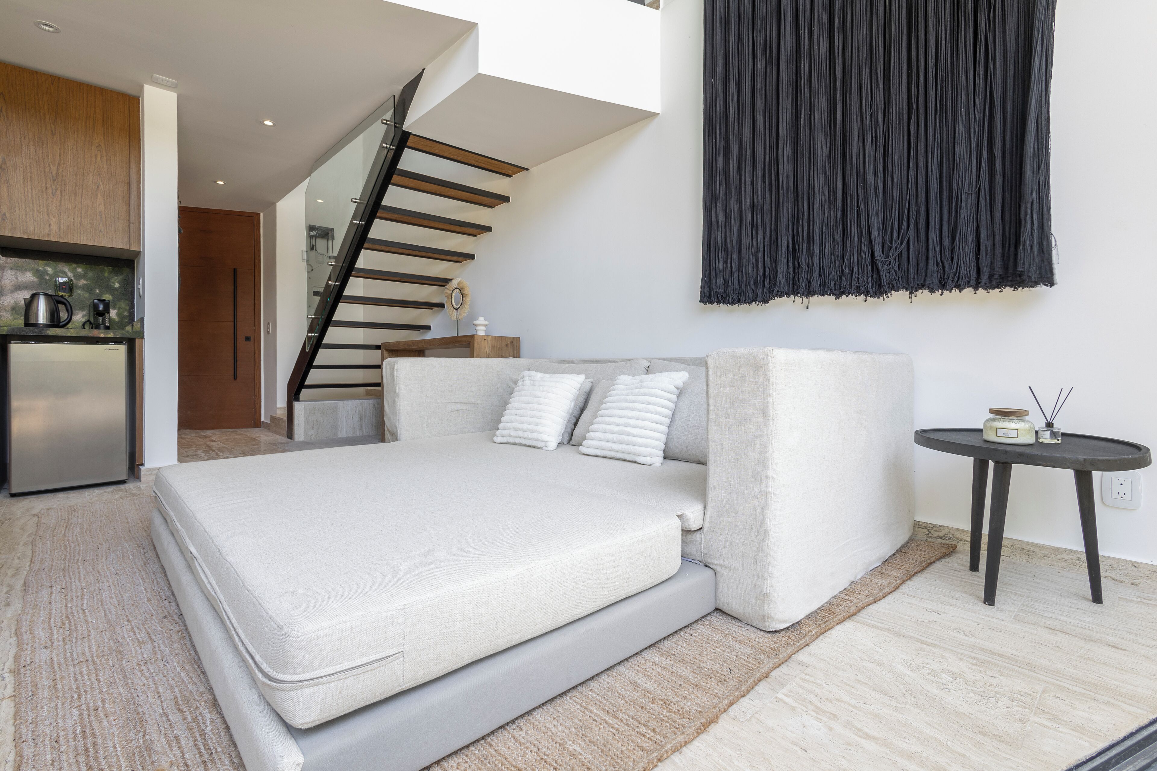 A modern bedroom with a sofa bed, a small table, a kitchen area, and a staircase.