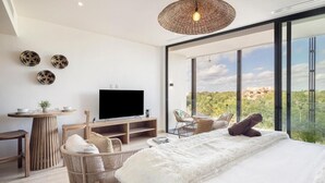 A modern bedroom with a large bed, a TV, wicker furniture, and a view of the landscape. - Mistiq Gardens 2 (Tulum)