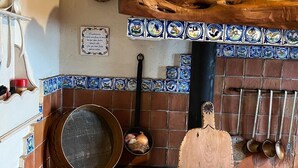 A rustic kitchen with a brick fireplace, a wooden cutting board, and a tiled backsplash.