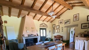 A rustic dining area with a wooden table, white chairs, a fireplace, and tiled flooring.