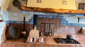 A kitchen with a brick backsplash, a wooden beam above the stove, and various cooking utensils hanging on the wall.