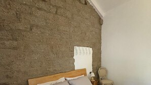 A bedroom with a stone wall, a wooden headboard, a bed with white bedding, a nightstand with a lamp, and a chair.