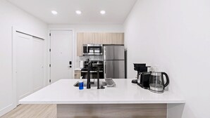 Una cocina moderna con armarios blancos, un refrigerador de acero inoxidable, una cafetera y un microondas.