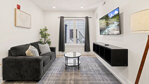 Una sala de estar moderna con sofá, una mesa de centro, televisor de pantalla plana y una escalera que lleva a un espacio al aire libre.