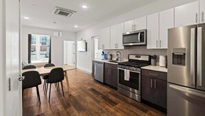 A modern kitchen with stainless steel appliances, a dining area with a wooden table and chairs, and a view of the outside. - Modern 3BD | Sleeps 8 | Northern Liberties (Philadelphia)