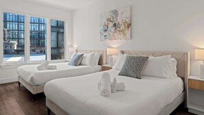 A hotel room with two beds, a large window, and a painting on the wall. - Modern 3BD | Sleeps 8 | Northern Liberties (Philadelphia)