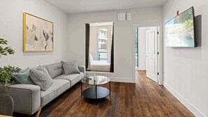 A modern living room with a grey sofa, a glass coffee table, and a painting on the wall. - Modern 3BD | Sleeps 8 | Northern Liberties (Philadelphia)