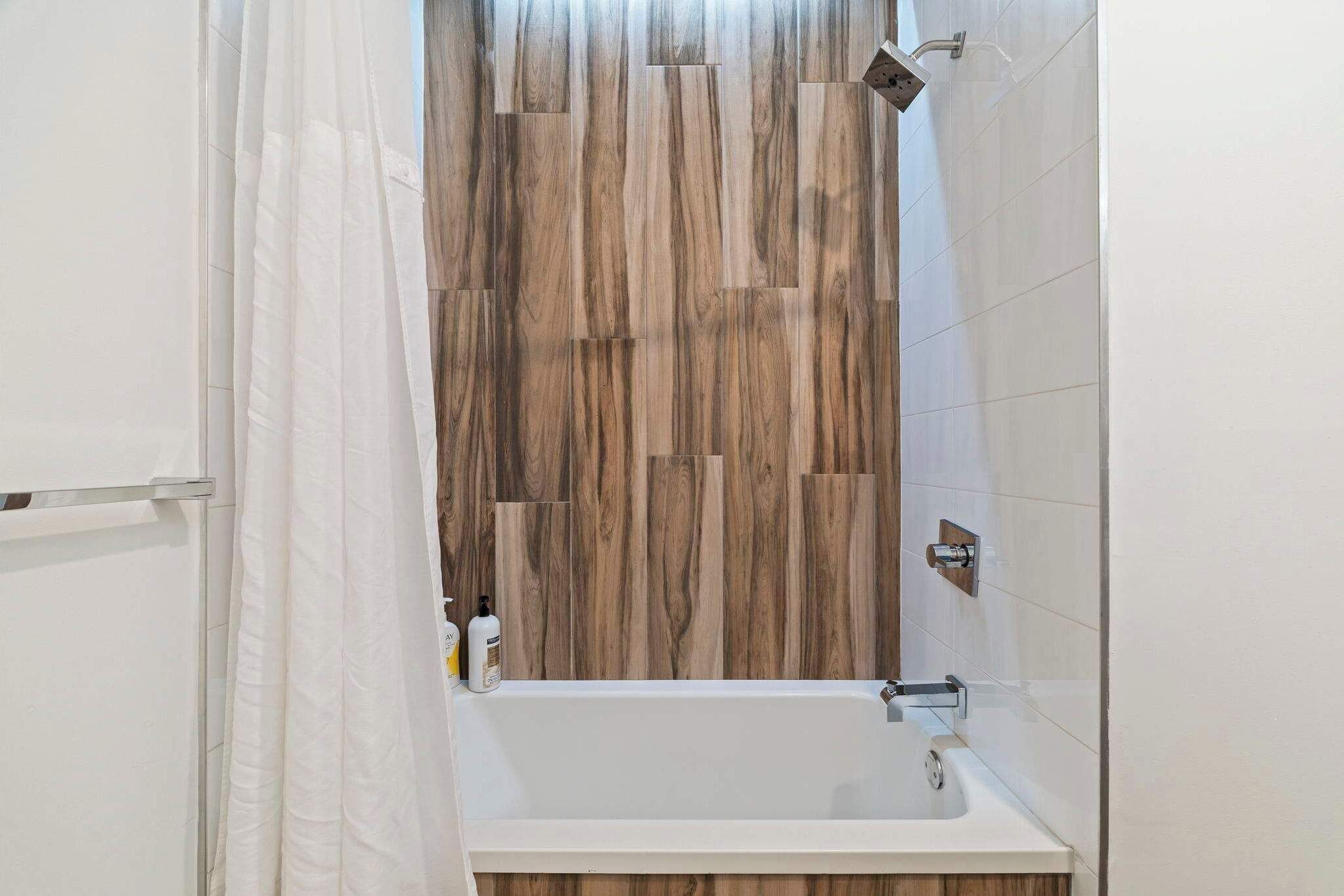 A bathroom with a wooden wall panel, a white bathtub, and a shower curtain.