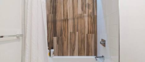 A bathroom with a wooden wall panel, a white bathtub, and a shower curtain.