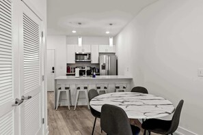 Une cuisine moderne avec des meubles blancs, des appareils en acier inoxydable et un îlot central doté de tabourets de bar.