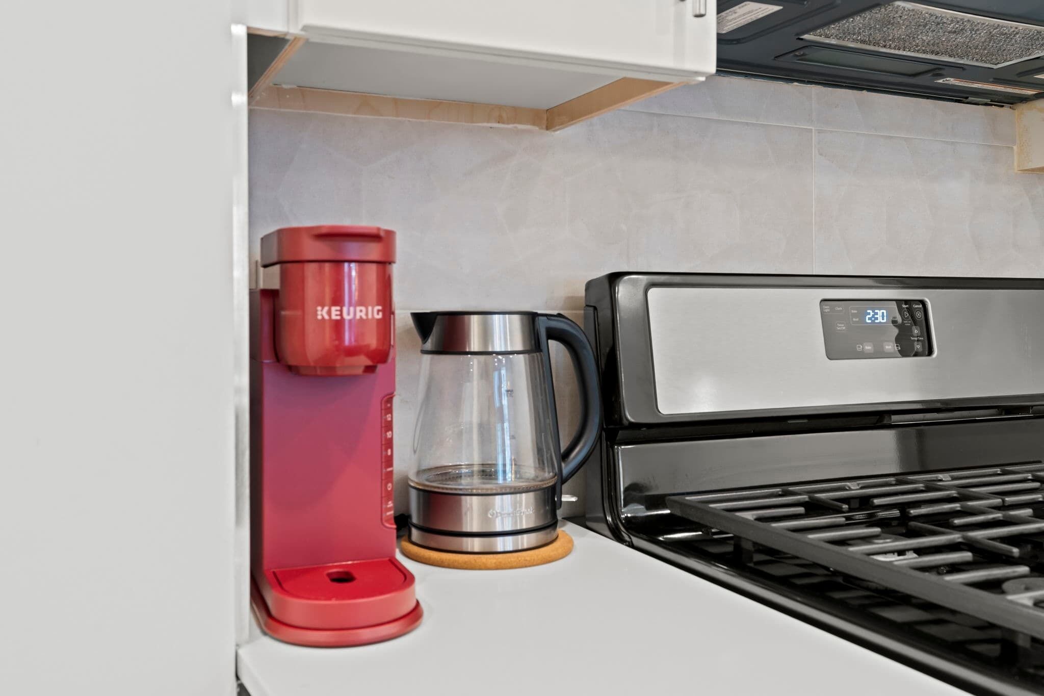 Ett kök med en Keurig-kaffemaskin, en glaskanna och en digital klocka som visar 2:30.