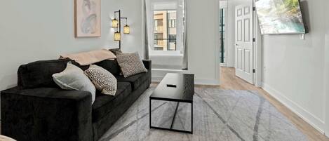 A modern living room with a dark sofa, a coffee table, and a large TV on the wall.