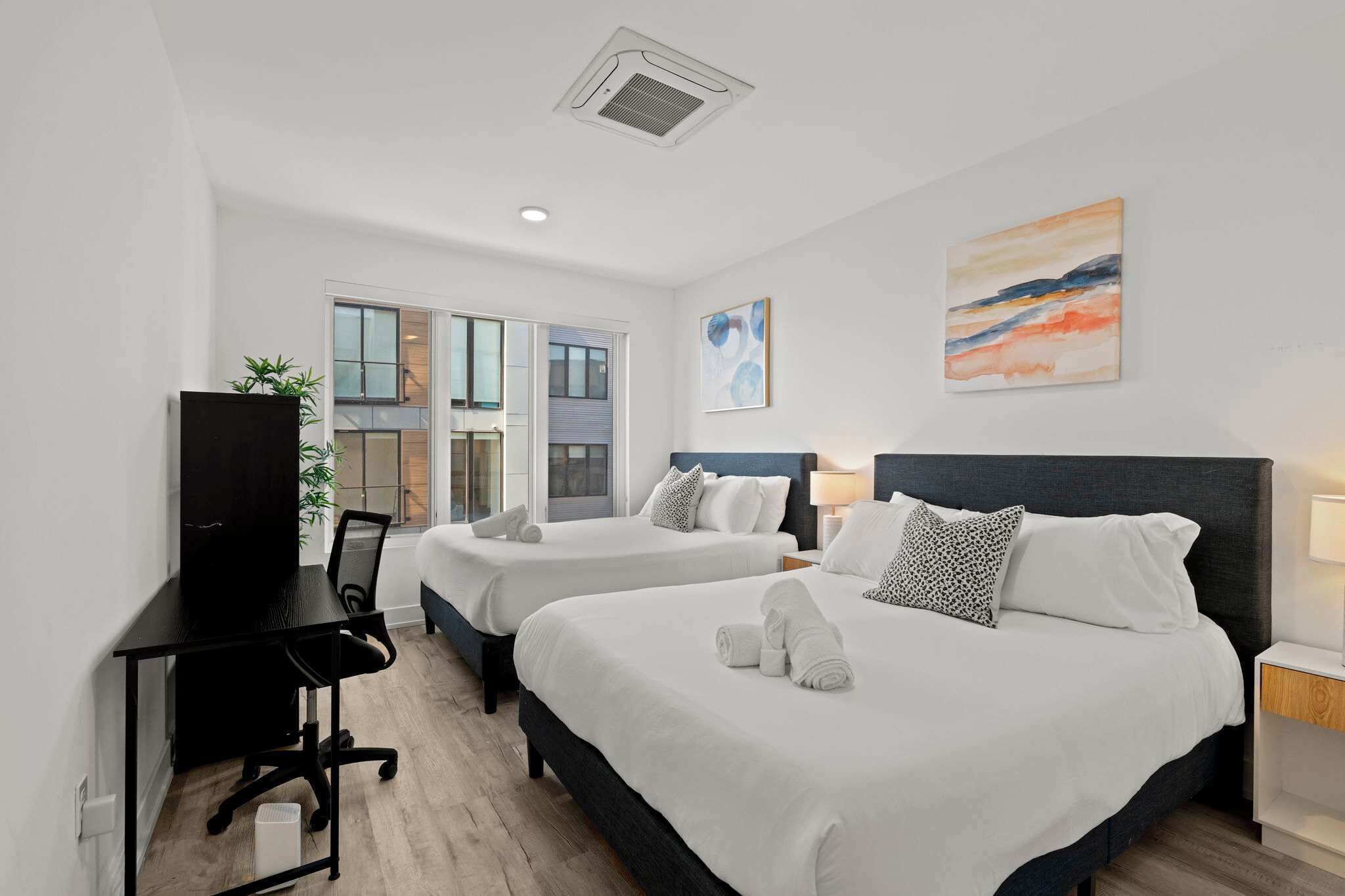 A hotel room with two beds, a desk, a TV, and a window with a view.