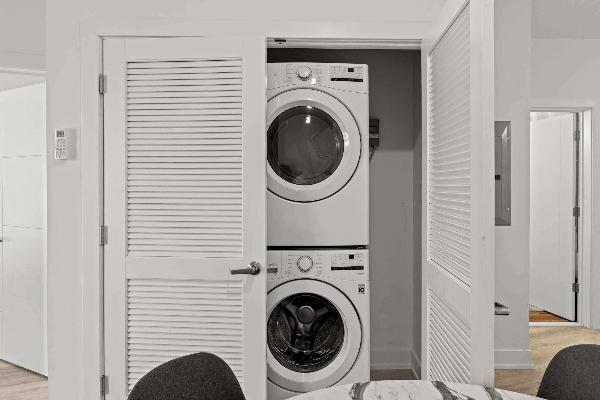 A laundry room with two stacked washing machines, a door with a handle, and a light switch on the wall.