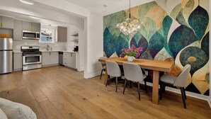 Une cuisine moderne avec un coin repas, une grande fresque murale abstraite et une table à manger en bois avec des chaises.