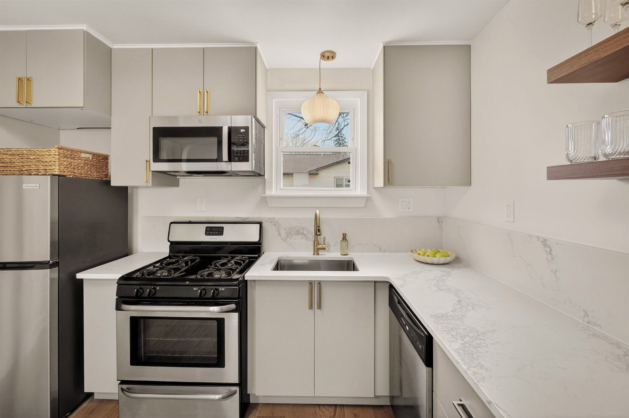 A modern kitchen with white cabinetry, stainless steel appliances, a window above the sink, and a hanging light fixture.
