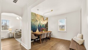 Un coin repas avec une table et des chaises en bois, un grand tableau abstrait accroché au mur et une vue sur l’extérieur par une fenêtre.