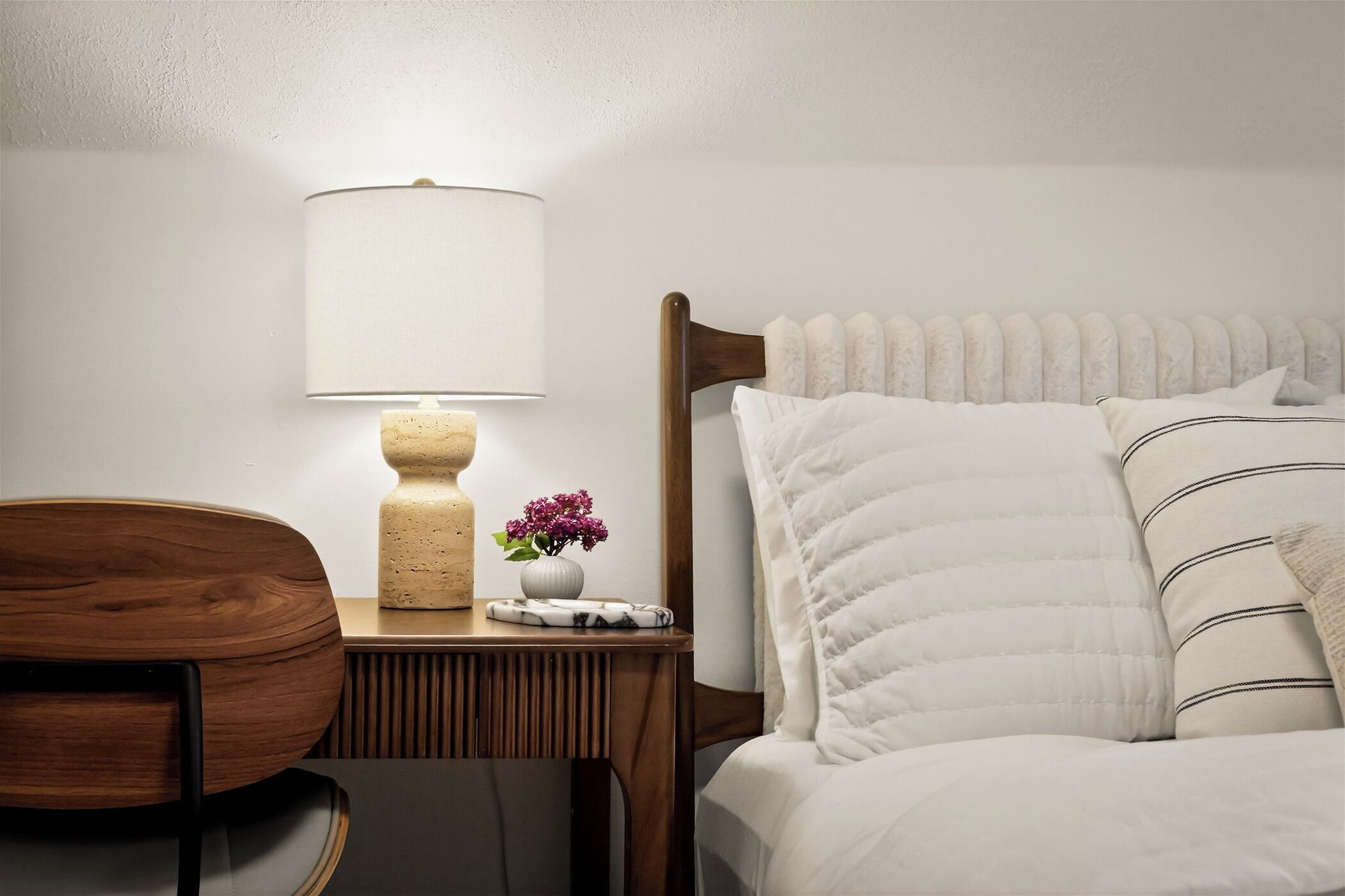 Une chambre bien rangée, avec un lit, une table de chevet, une lampe et une chaise.