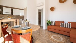Un moderno salón con una mesa redonda de madera, sofá naranja y una cocina al fondo.