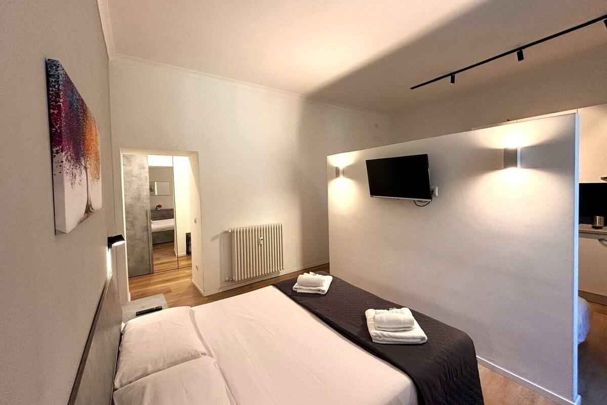 Une chambre d’hôtel moderne équipée d’un lit, d’un téléviseur à écran plat fixé au mur, d’un radiateur et d’une porte donnant sur une autre pièce.