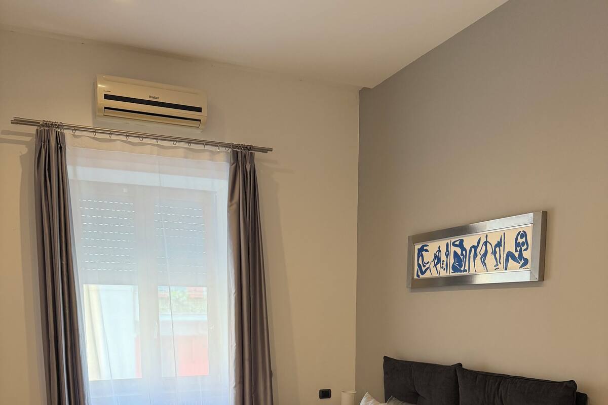 Une chambre à coucher comprenant un lit, des rideaux, un appareil de climatisation et une œuvre d’art accrochée au mur.