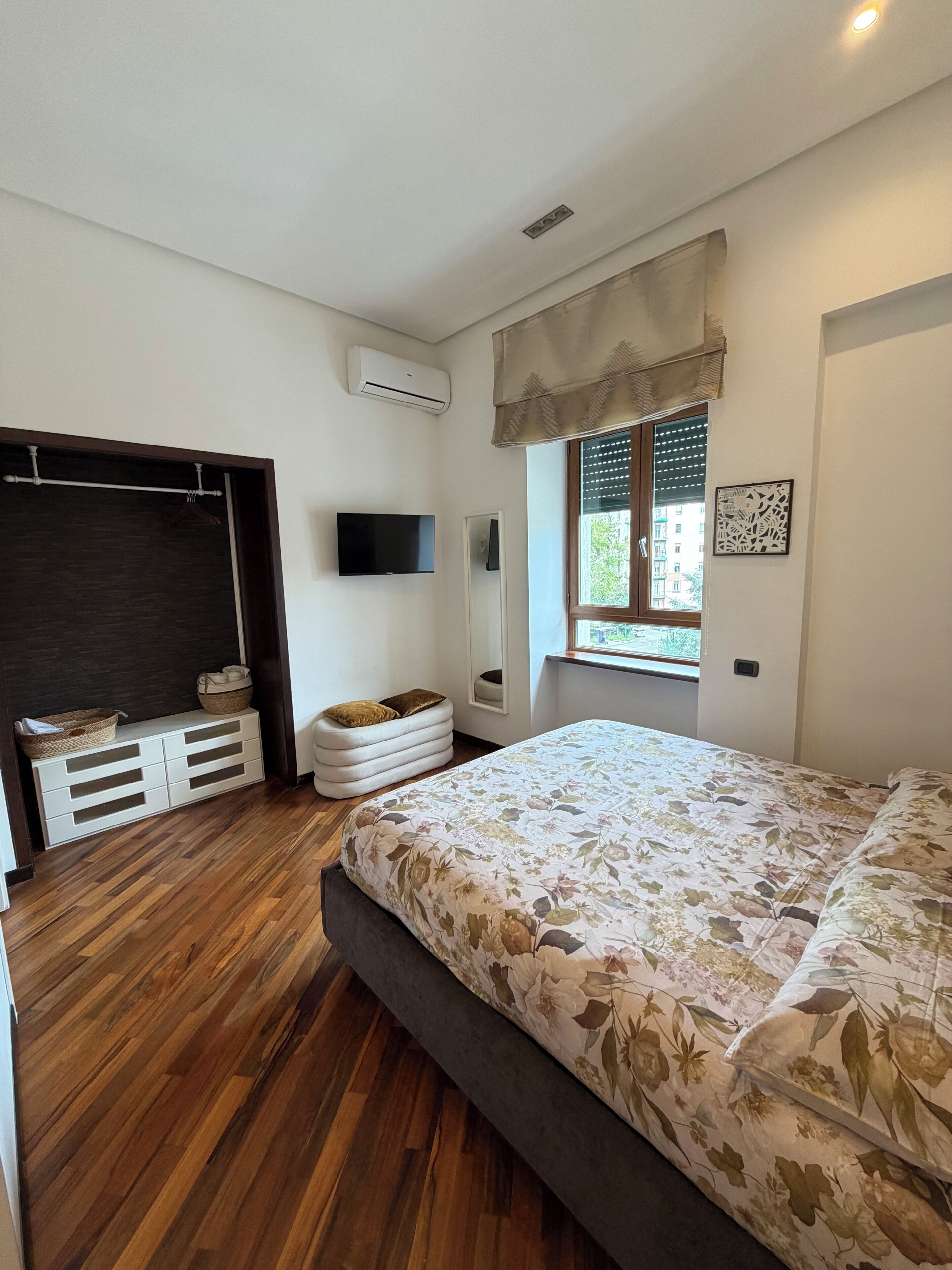 Une chambre à coucher comprenant un lit, une télévision, une fenêtre avec des stores, une armoire et une table de chevet.