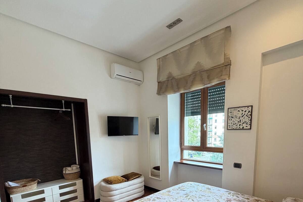Une chambre à coucher comprenant un lit, une télévision, une fenêtre avec des stores, une armoire et une table de chevet.
