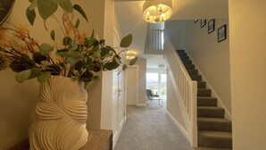 Un couloir avec un escalier, un vase avec des plantes et un lustre.