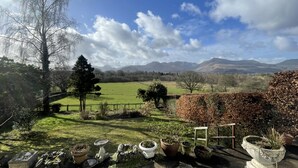 Un jardin agrémenté de plantes en pot, d’un banc en bois et offrant une vue sur des collines lointaines.