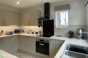 Una cucina moderna con mobili chiari, una cappa aspirante nera, forno integrato, lavello in acciaio inossidabile e una finestra con vista.