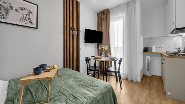 Pieni hotellihuone, jossa on sänky, pieni ruokailutila, minikeittiö ja televisio.