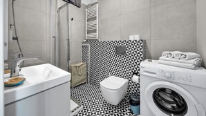 Moderni kylpyhuone, jossa on suihku, wc, pesuallas ja pesukone.
