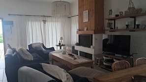 Un salon comprenant un canapé, un téléviseur, une table basse en bois et un coin repas avec des chaises.