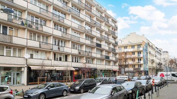 A multi-story residential building with balconies, a ground-level shop, and parked cars along the street. - Wilcza Retro – City Center, Balcony – by Rentujemy (Warszawa)